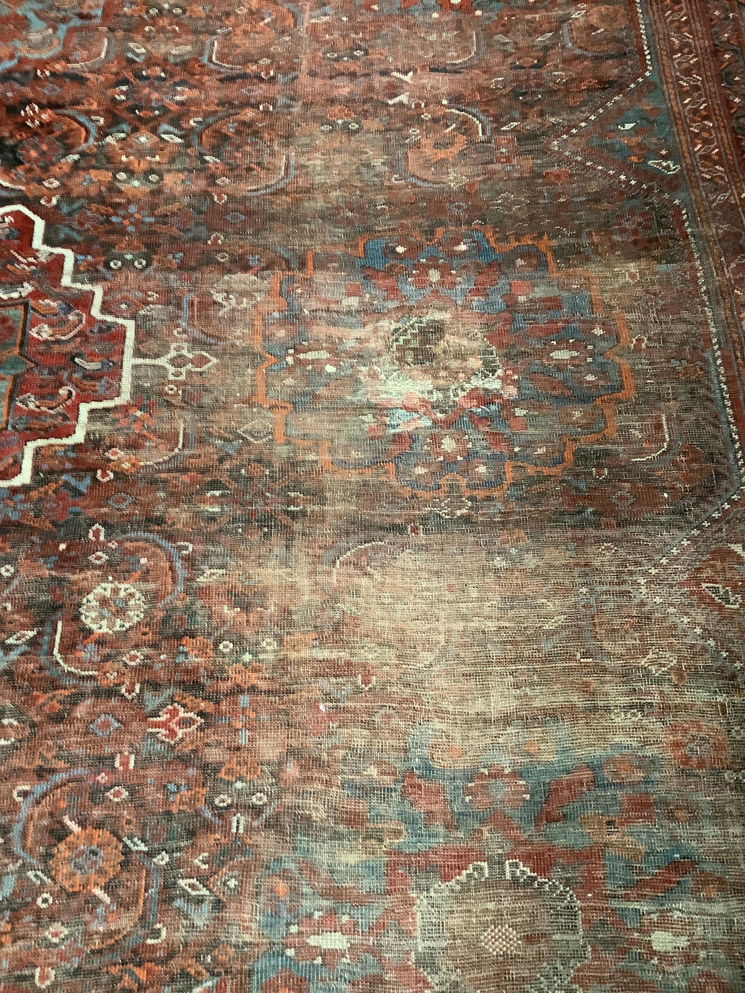 An early 20th century North West Persian red ground carpet, 410 x 348cm, worn and patch repaired.